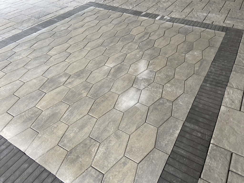A close-up of a patterned pavement featuring hexagonal gray tiles bordered by rectangular ones, creating a geometric design. No people or landmarks visible.
