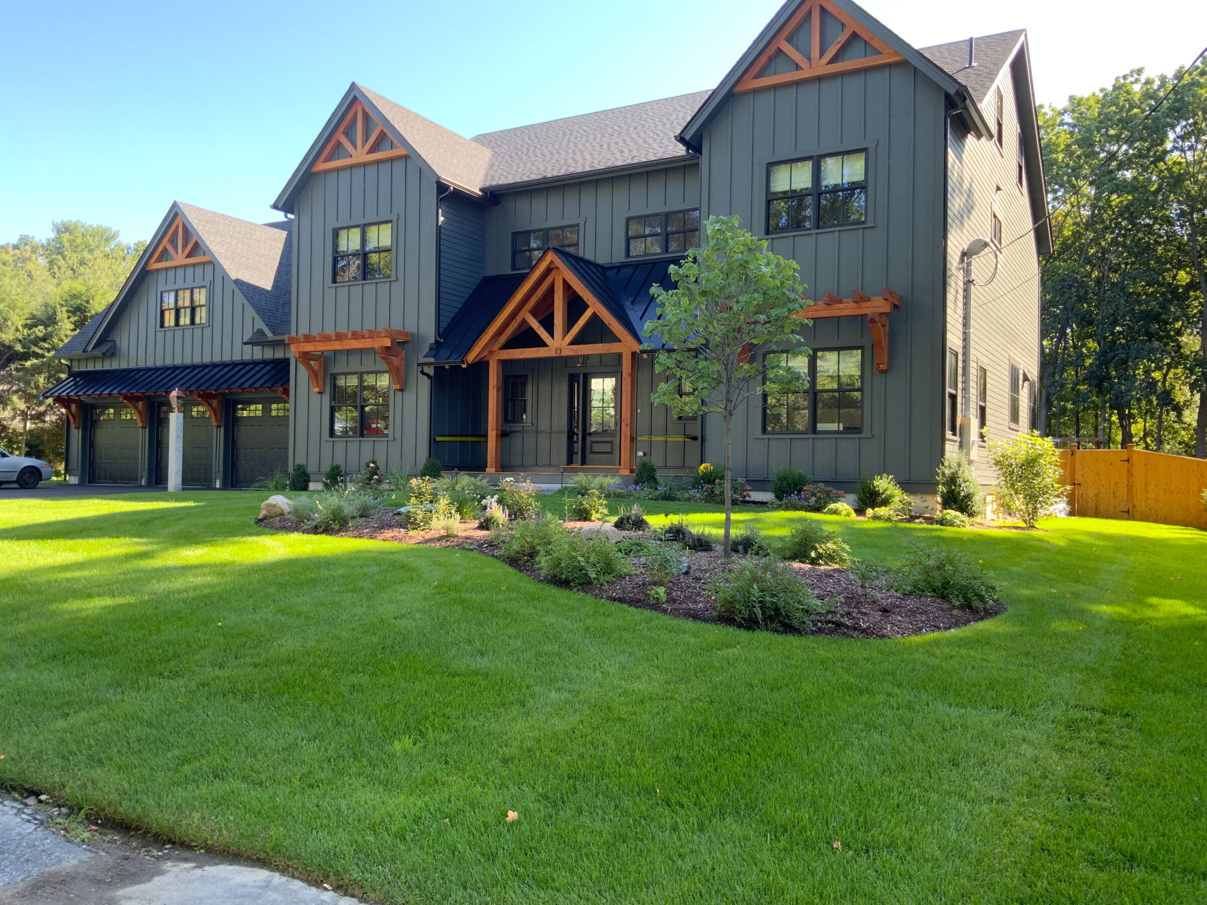 Two-story house with dark siding, wood accents, and a well-maintained lawn in a suburban setting. No people or notable landmarks visible.