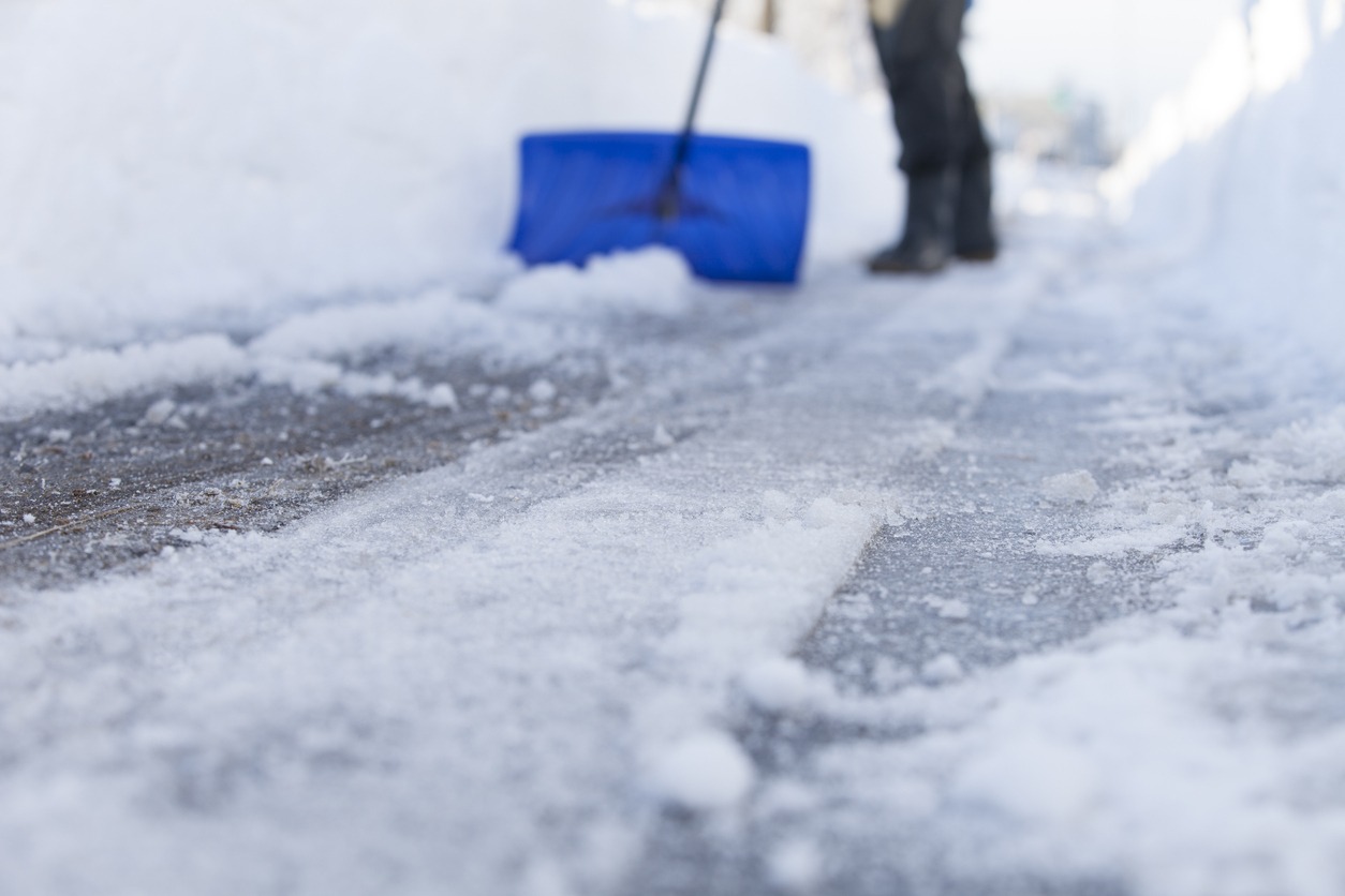 A person shovels a snowy pathway with a blue shovel, clearing ice and snow, emphasizing winter effort and outdoor activity.