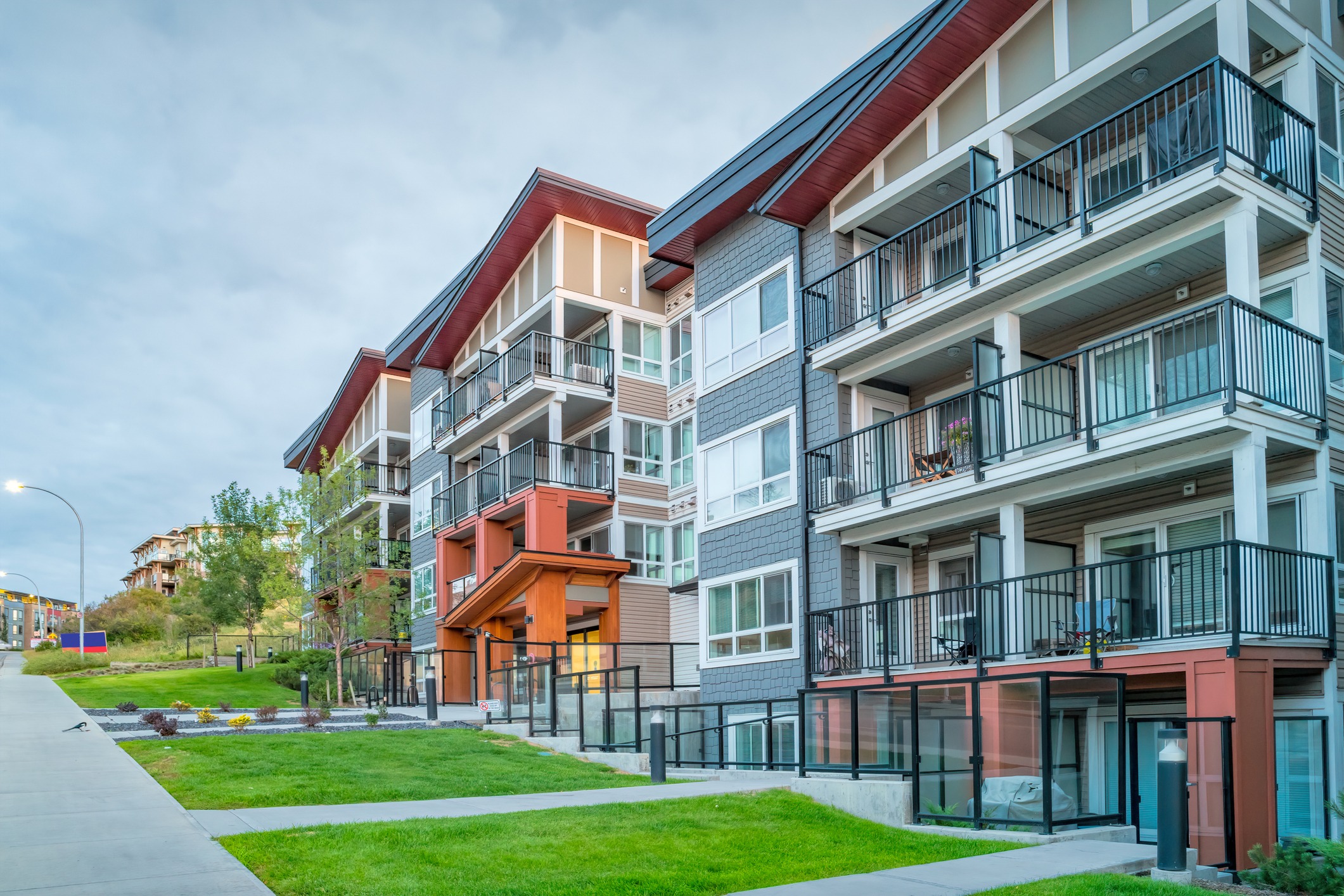 Modern, multi-story apartment building with balconies, surrounded by green lawns and trees. No recognizable landmarks or historical buildings are present.