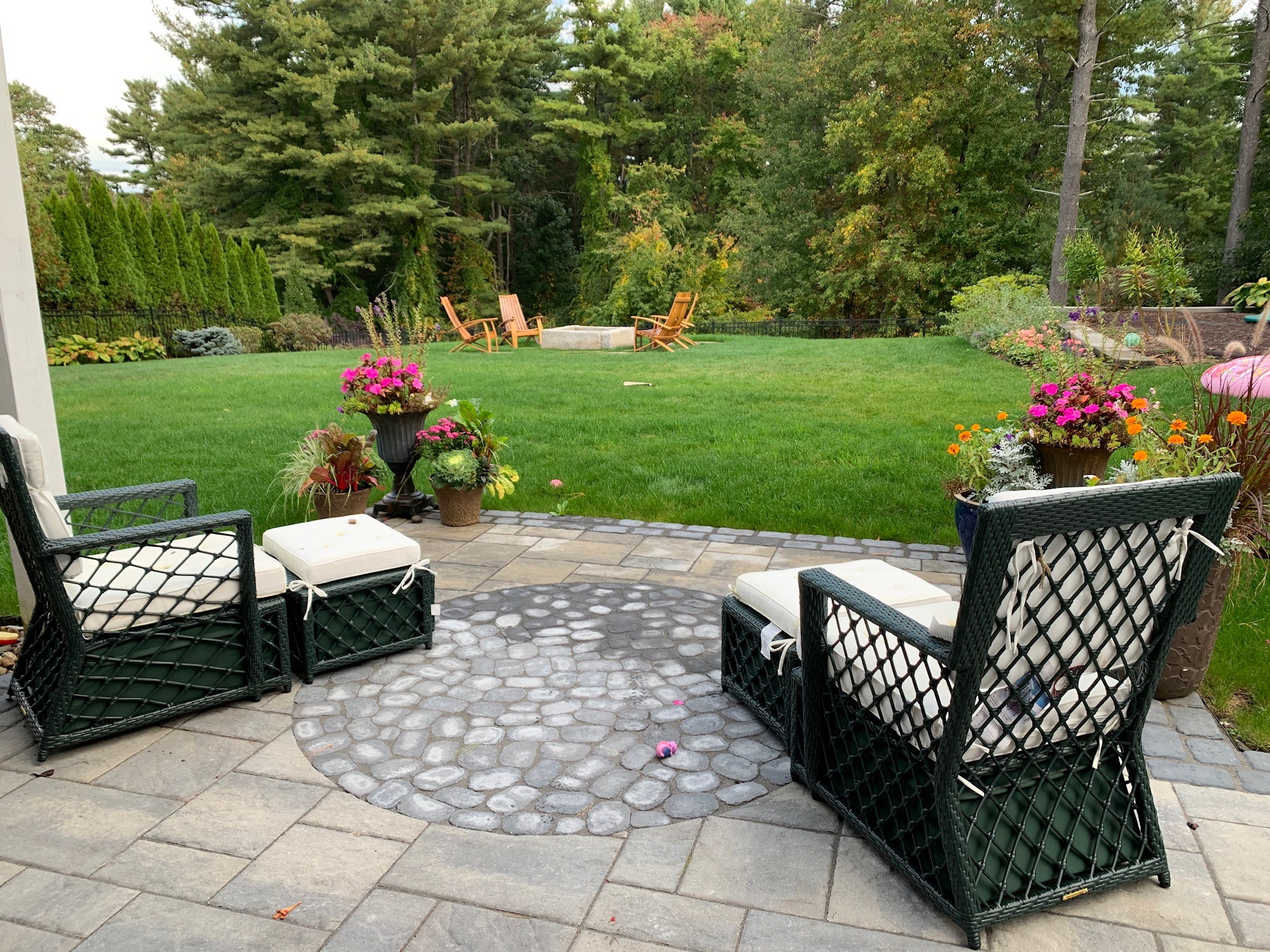 A peaceful garden patio with chairs, surrounded by vibrant flowers, overlooks a lush lawn with trees in the background.